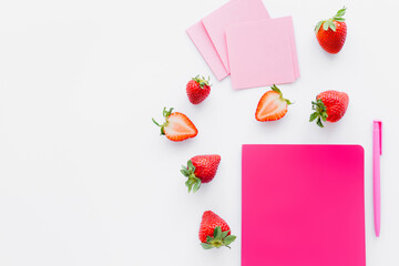 Top view of ripe strawberries near notebook and sticky notes on white background.
