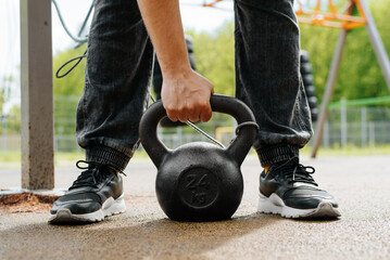Obraz premium Close-up of a male athlete lifting a heavy weight while standing on a sports field in the park. Weightlifting workout outdoors.