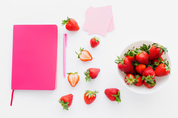 Top view of pink notebook and fresh strawberries on white background.