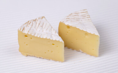 Two slice of round brie cheese out over white corrugated background.
