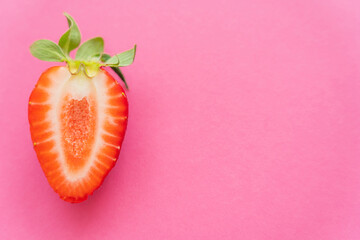 Close up view of half of strawberry on pink background.