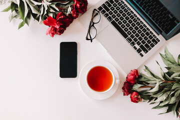 Workplace top view, laptop, cup of tea, phone, peonies, glasses