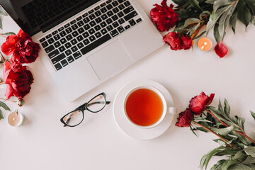 Top view female workplace, laptop, cup of tea, peonies, glasses
