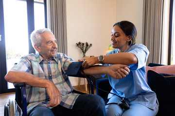Biracial female doctor examining caucasian senior man's blood pressure with stethoscope and gauge