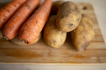 young potatoes and carrots lie on the surface of a wooden table in the kitchen. Potato and carrot supply problems, sales restrictions, global famine, potato shortage