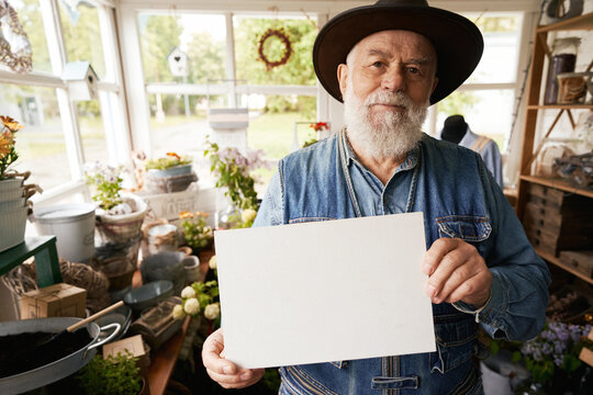 Aged florist holding empty paper with copy space in shop
