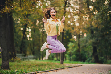 Full length body size view of attractive funky cheerful girl jumping having fun showing v-sign fooling outdoors