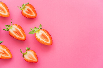 Flat lay of cut fresh strawberries on pink background.