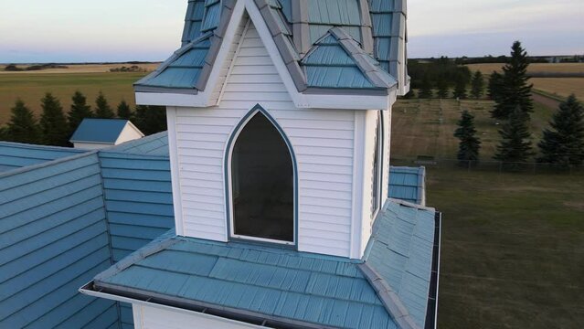 The bell inside a pristine white steeple of a wooden countryside church in rural Alberta, Canada at sunset. Close up orbiting aerial footage