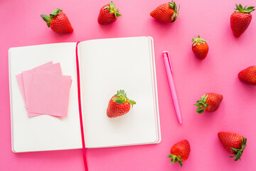 Top view of notebook and sticky notes near fresh strawberries on pink background.