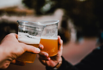 two plastick glass of beer in hand. Beer clinking outdoor