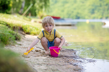 Little toddler child, cute boy, playing with toys in the sand on a lake