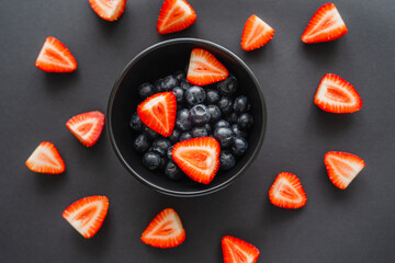 Top view of blueberries in bowl near strawberries on black background.