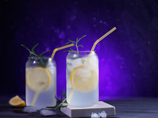 Two glasses of refreshing summer cocktail with gin and tonic, lemon and rosemary. neon backlit background