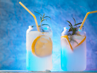 Two glasses of cold summer lemonade or cocktail with gin and a sprig of rosemary. Neon background