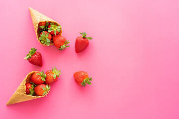 Top view of juicy strawberries in sweet waffle cones on pink background.