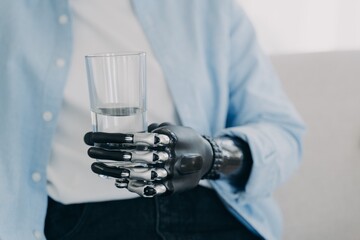 Morning routines of disabled person. Girl is holding glass of water with robotic arm prosthesis.