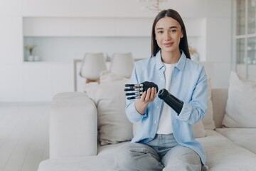 Positive disabled young woman is disassembling bionic arm prosthesis and smiling.