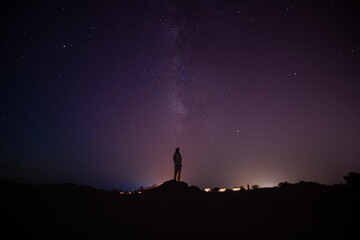silhouette of a person standing on a rock looking at stars and milky way 