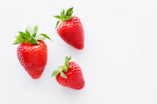 Top view of ripe strawberries with leaves on white background.