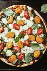 Pizza with cherry tomatoes, mozzarella and basil pesto. Dark wooden background. Top view.