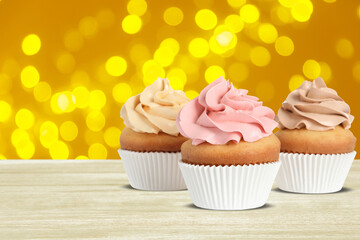 Delicious birthday cupcakes on white wooden table against blurred lights. Space for text