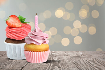 Sweet birthday cupcakes on wooden table against blurred lights. Space for text