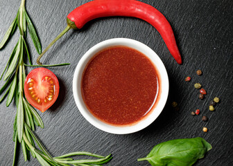 Grill sauce in bowl on a slate slab  with chili peppers and spices on black background