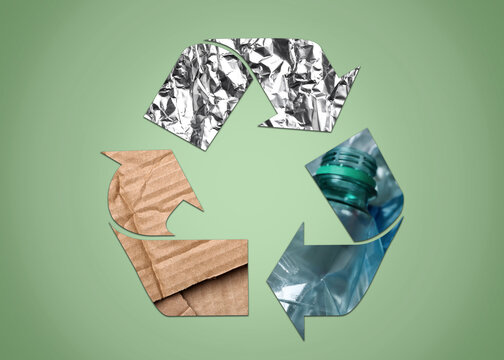Recycling symbol made of crumpled foil, plastic bottles and cardboard on light green background