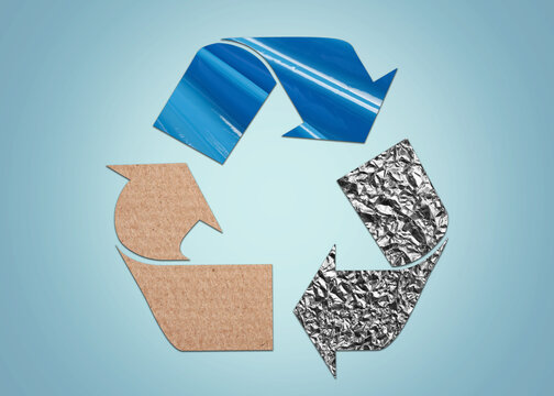 Recycling symbol made of crumpled foil, cardboard and turquoise stretch wrap on light blue background