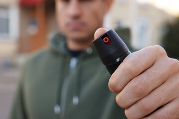 Man using pepper spray outdoors, focus on hand. Space for text