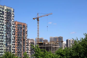 Fototapeta na wymiar View to construction cranes, new residential buildings and green trees. Real estate in summer