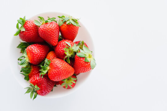 Top view of strawberries in bowl on white background.