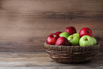 Fresh ripe green and red apples with water drops in wicker bowl on wooden table, space for text