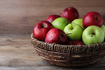 Fresh ripe green and red apples with water drops in wicker bowl on wooden table