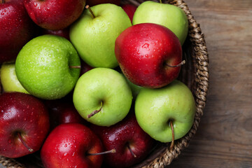 Fresh ripe green and red apples with water drops in wicker bowl on wooden table, top view