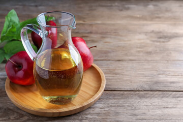 Jug of tasty juice and fresh red apples on wooden table, space for text