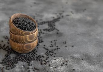 Fototapeta na wymiar Wooden bowls of dry black lentils beans on grey table close up, protein source for vegetarian diet