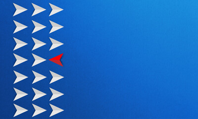 Business concept of innovation and solution with a set of white paper planes moving in one direction and one red paper plane flying opposite it on a blue background.
