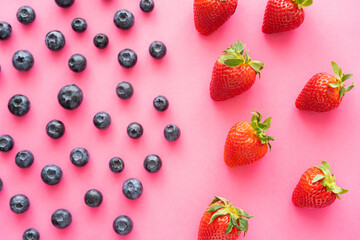 flat lay of juicy blueberries near strawberries on pink background.