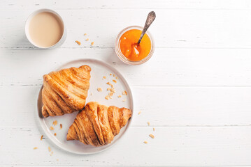 Plate with two fresh croissants, jam and coffee on white wooden table. Top view.