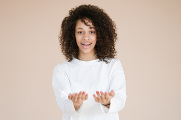 Portrait of smiling, pleasant African american girl studio portrait isolated on brown background showing something on the palms of her open two hands holding for object copy 