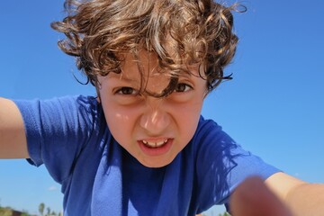 Selective focus to excited emotion face of arabian preschooler boy with big hazel eyes on blurred blue sky background. Portrait of irritated little kid boy. Behavioral children issues.