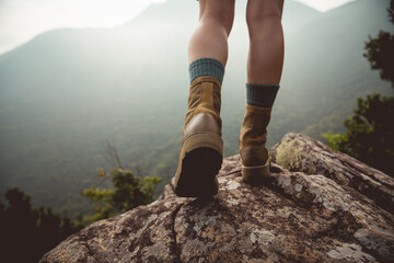 Suceesful woman hiker legs stand on mountain peak cliff edge