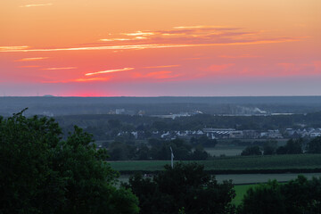 A wonderful sunset with a few fluffy clouds, covering the rolling hills of south Limburg in the Netherlands with an orange and golden glow, creating a magical atmosphere over the agricultural fields.