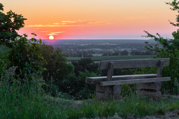 Fototapeta na wymiar A beautiful sunset late Spring over the rolling hills from south Limburg. The wooden bench is an idyllic place for couples to enjoy a romantic evening overlooking to landscape.
