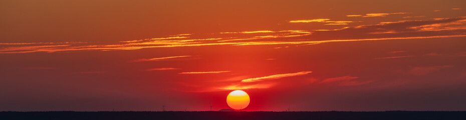 An amazing African sunset over the rolling hills of south Limburg, with the sun as a yellow ball of fire and an orange sky with a few fluffy clouds for some contrast in the sky