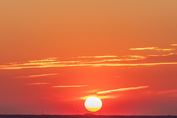 An amazing African sunset over the rolling hills of south Limburg, with the sun as a yellow ball of fire and an orange sky with a few fluffy clouds for some contrast in the sky