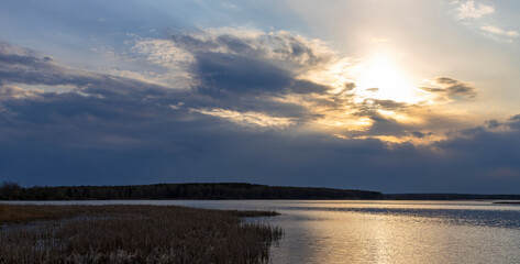 Evening dramatic landscape, lake in spring, sun shining through blue clouds. Ripples on the water from a strong wind.