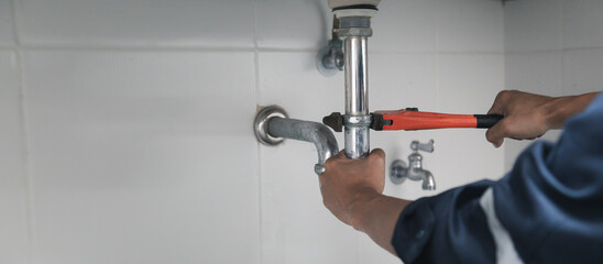 Male Plumber Using Wrench To Fix Leaking Sink In Home Bathroom.